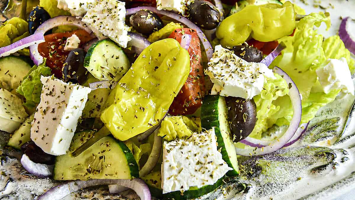 Greek salad with feta cheese, olives, cucumbers, tomatoes, red onion, lettuce, herbs, and yellow peppers.