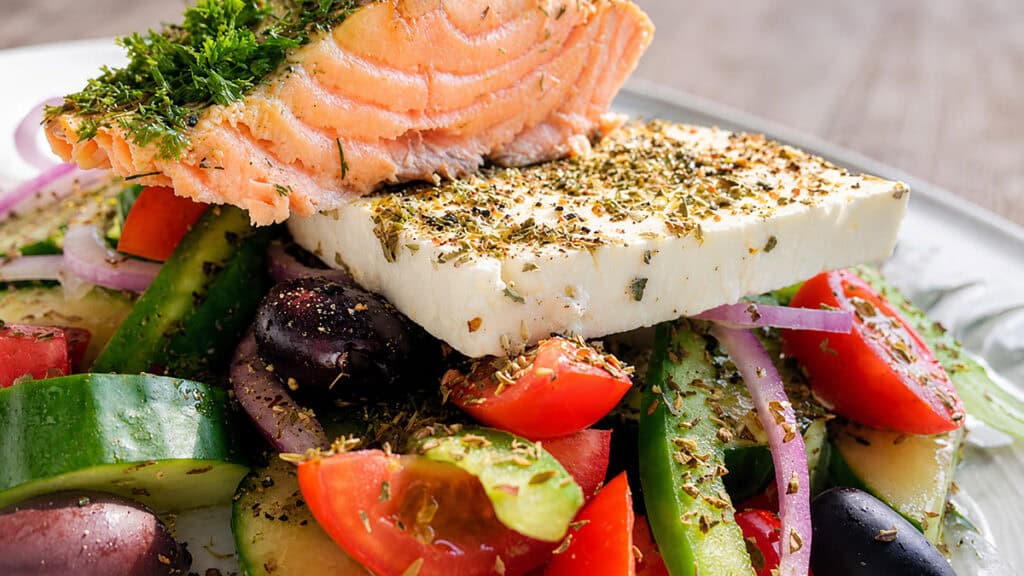 Greek salad with feta cheese, salmon, tomatoes, cucumbers, olives, red onion, and herbs.