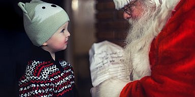 Toddler in black sweater standing in front of Santa Claus