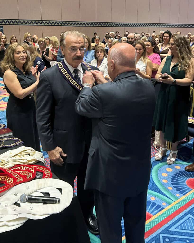 E. Chris Kaitson receives the AHEPA President’s jewels during the installation ceremony at the 103rd Supreme Convention, surrounded by delegates and family members.