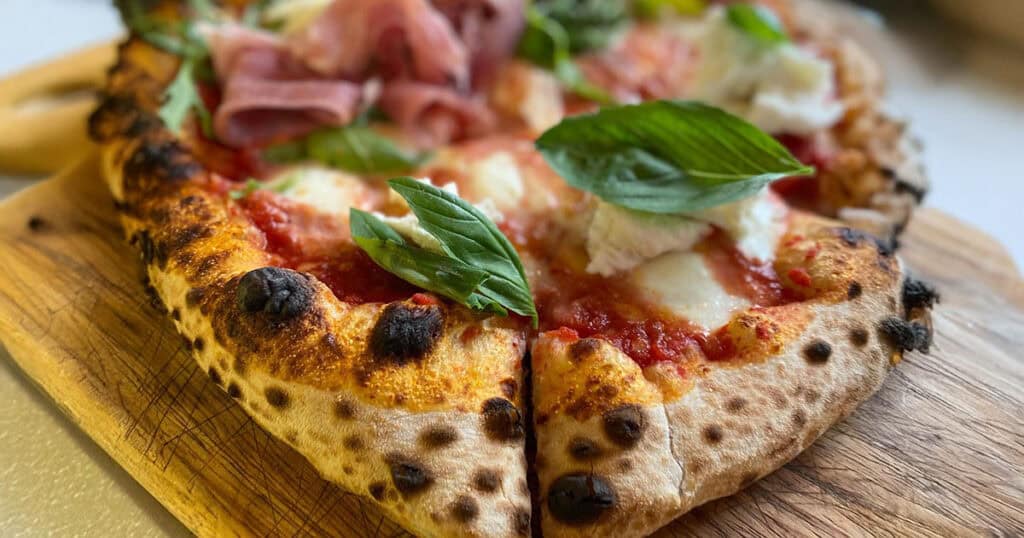 Close-up of a Neapolitan-style pizza with fresh basil and cured meat at Salento in Thessaloniki.