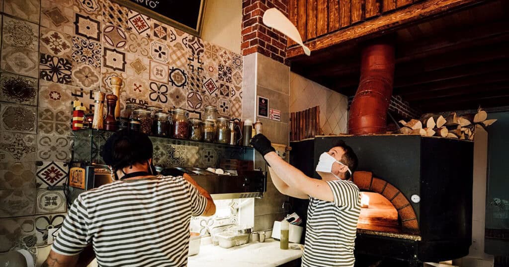 Pizza makers at Salento tossing dough by hand in front of a wood-fired oven.