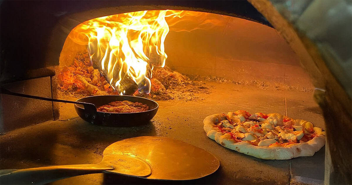 Wood-fired pizza baking next to a pan of sauce inside a traditional oven at Salento, Thessaloniki