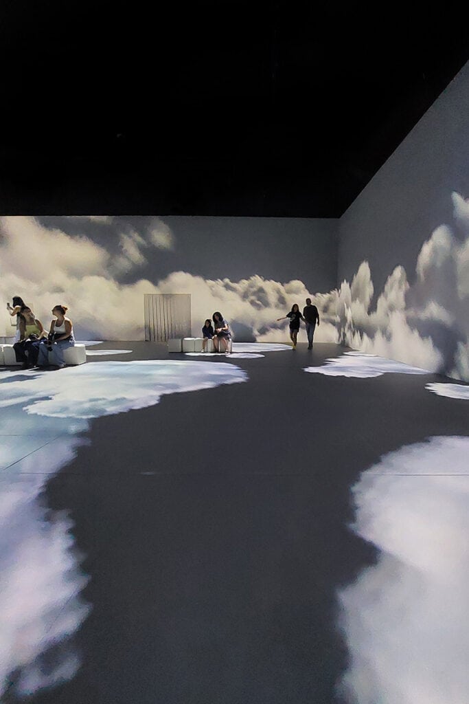 Visitors inside Frida Kahlo immersive exhibition with clouds projected on the floor and walls
