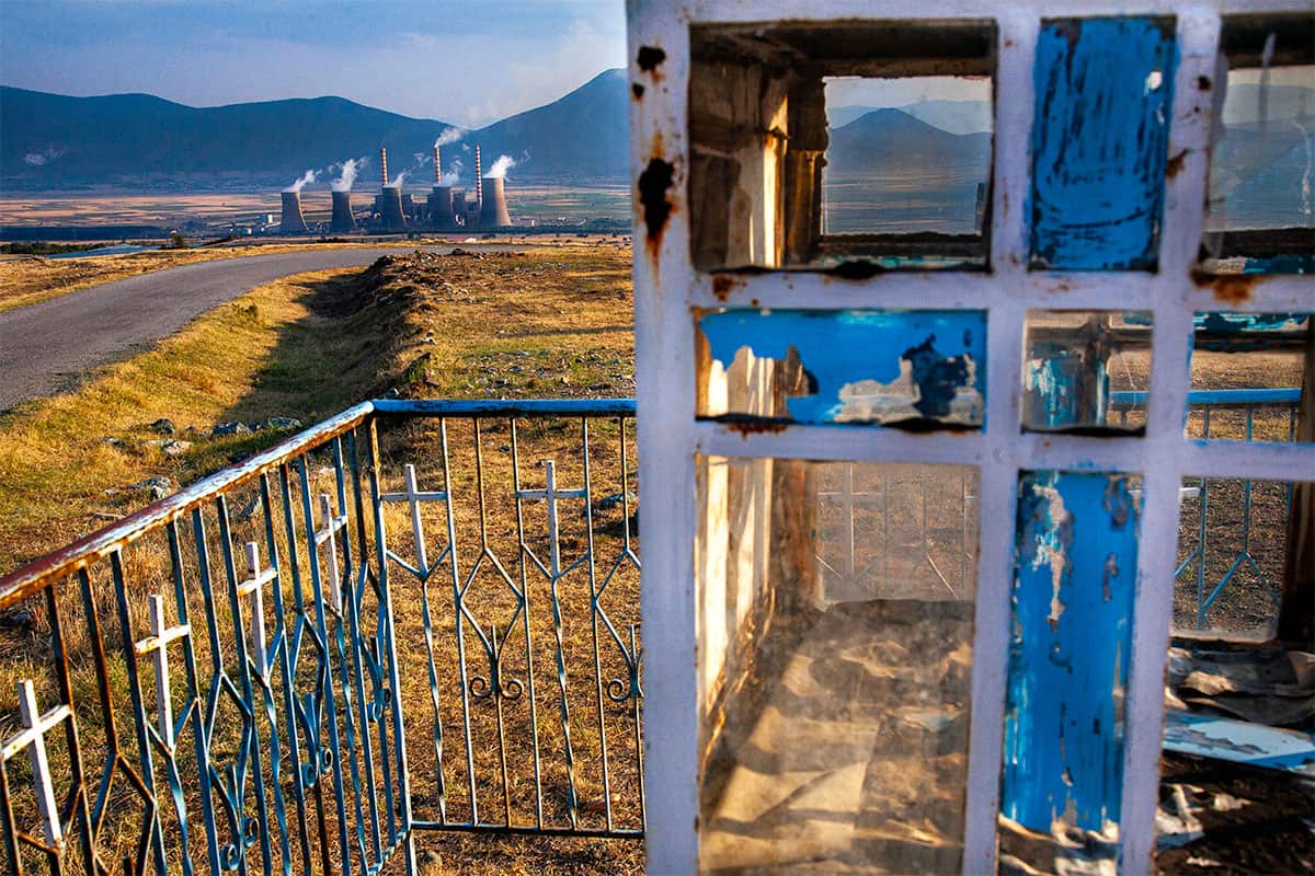 Through the broken windows of a roadside pareklisi, the coal towers of Ptolemaida rise in the distance
