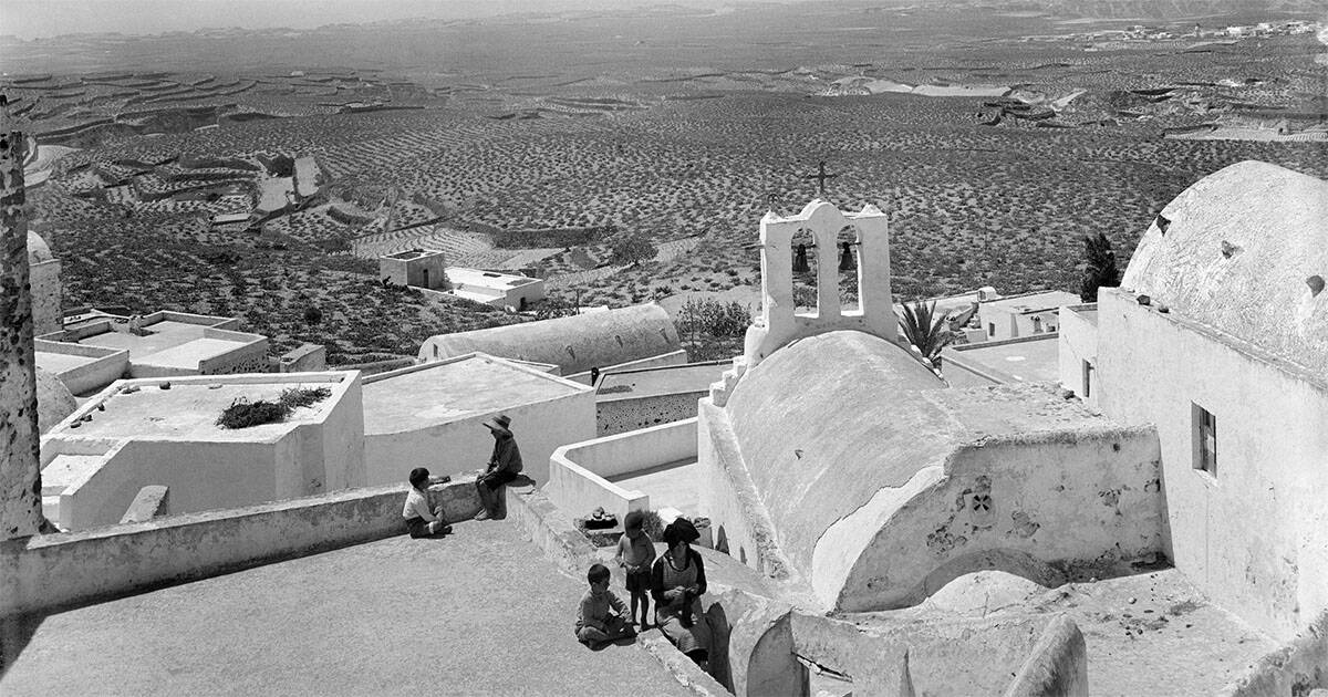 View over Pyrgos rooftops with villagers and children near a church, Santorini, ca. 1930