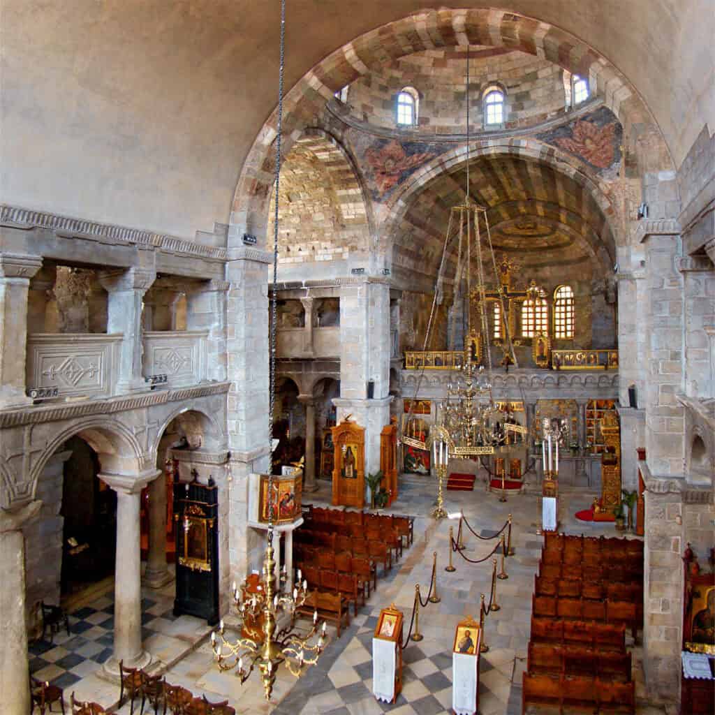 Interior view of Panagia Ekatontapiliani, a historic Byzantine church in Paros, Greece, showing stone arches, chandeliers, and iconostasis.