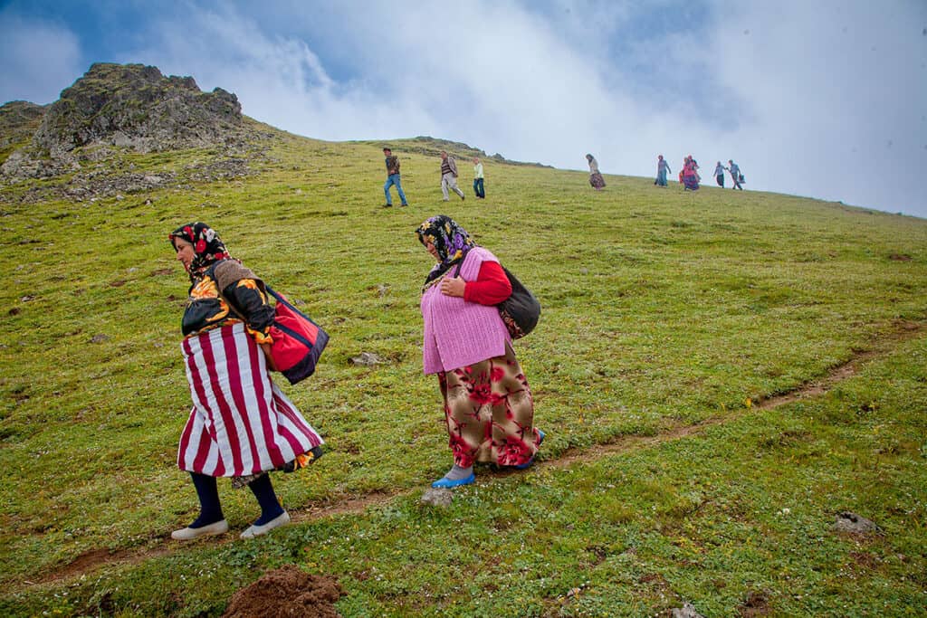 Women in patterned dresses and headscarves walk down a grassy slope in Kadırga Yaylası, Turkey.