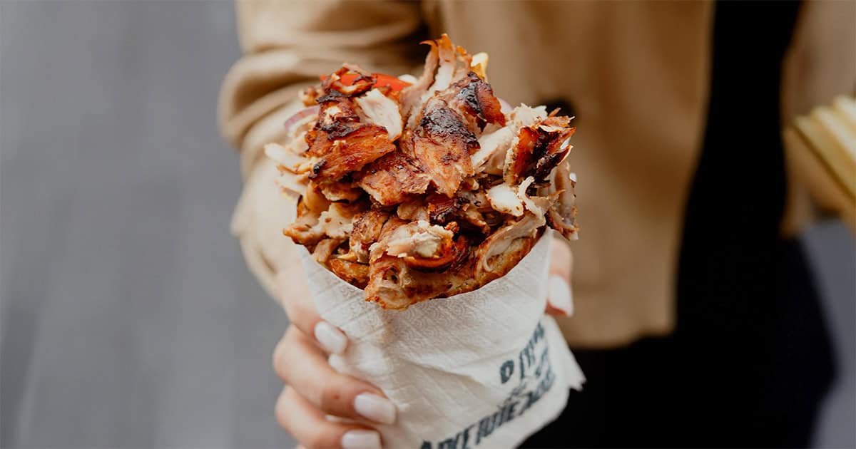 Close-up of a hand holding an overstuffed gyro with grilled meat from "O Gyros tis Aristotelous" in Thessaloniki