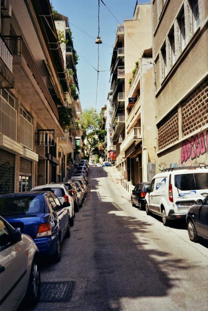 Narrow uphill street in Athens lined with parked cars on both sides