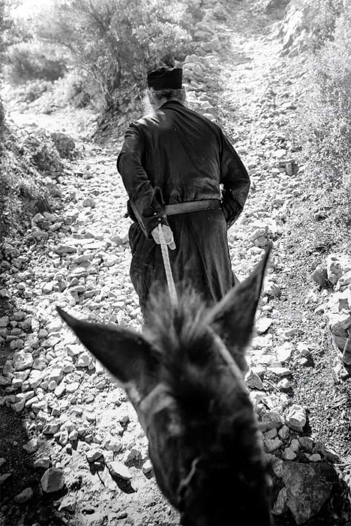 Monk leading a donkey up a rocky mountain path in Mount Athos.