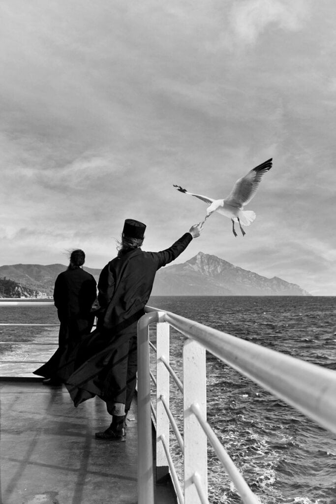 Monk feeding a seagull while crossing by ferry to Mount Athos.