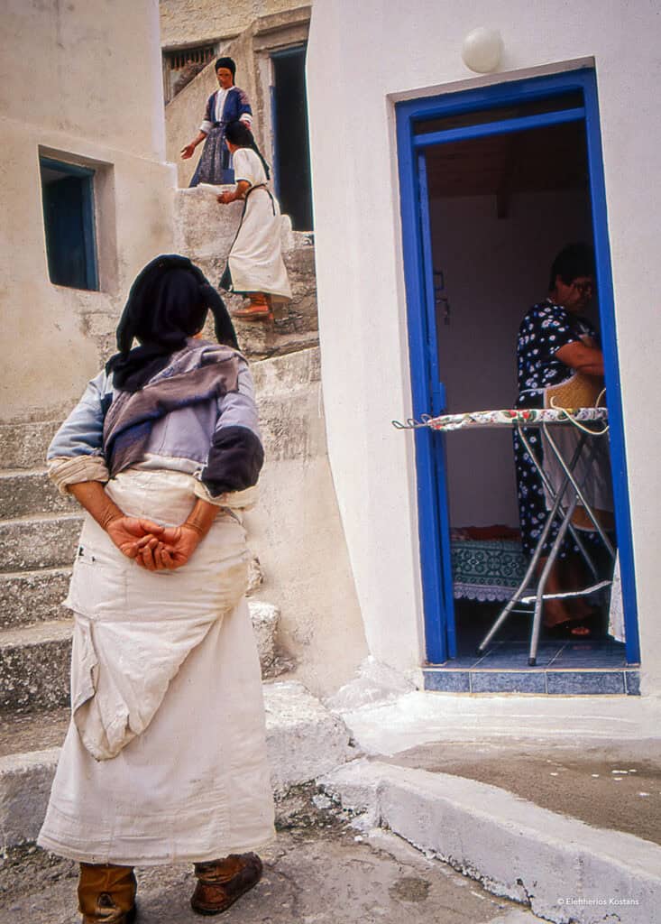 Women in traditional dress chatting on the stone steps of a whitewashed alley in Olympos