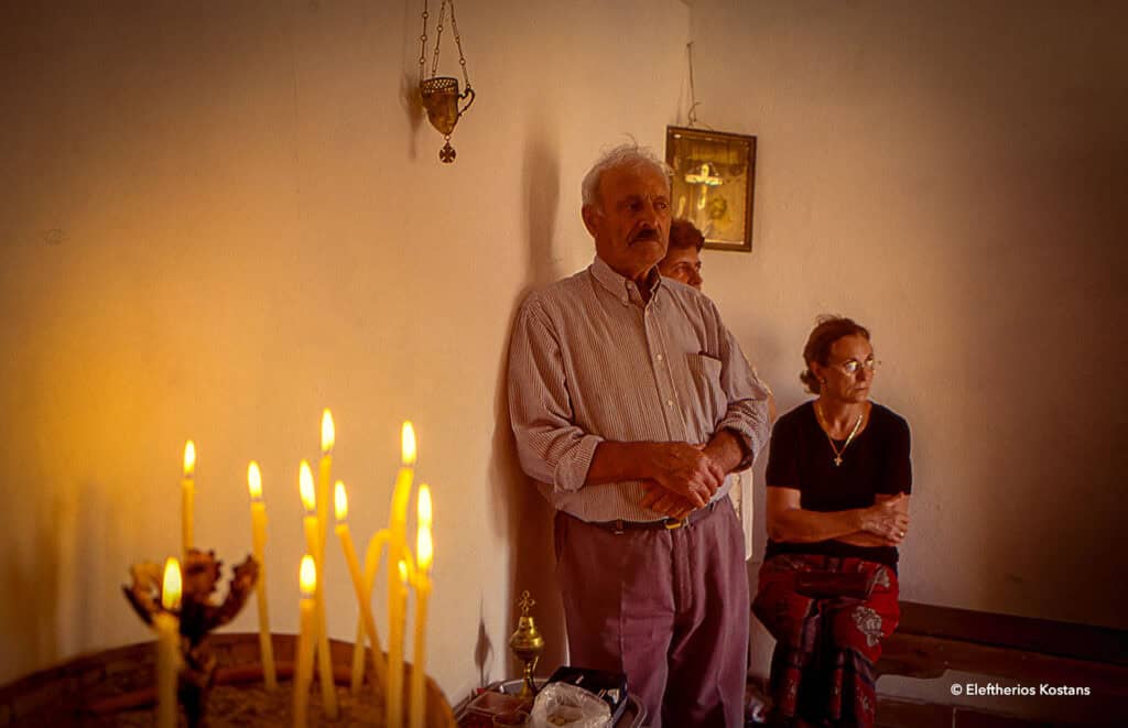 Villagers standing beside lit candles inside a small church in Olympos