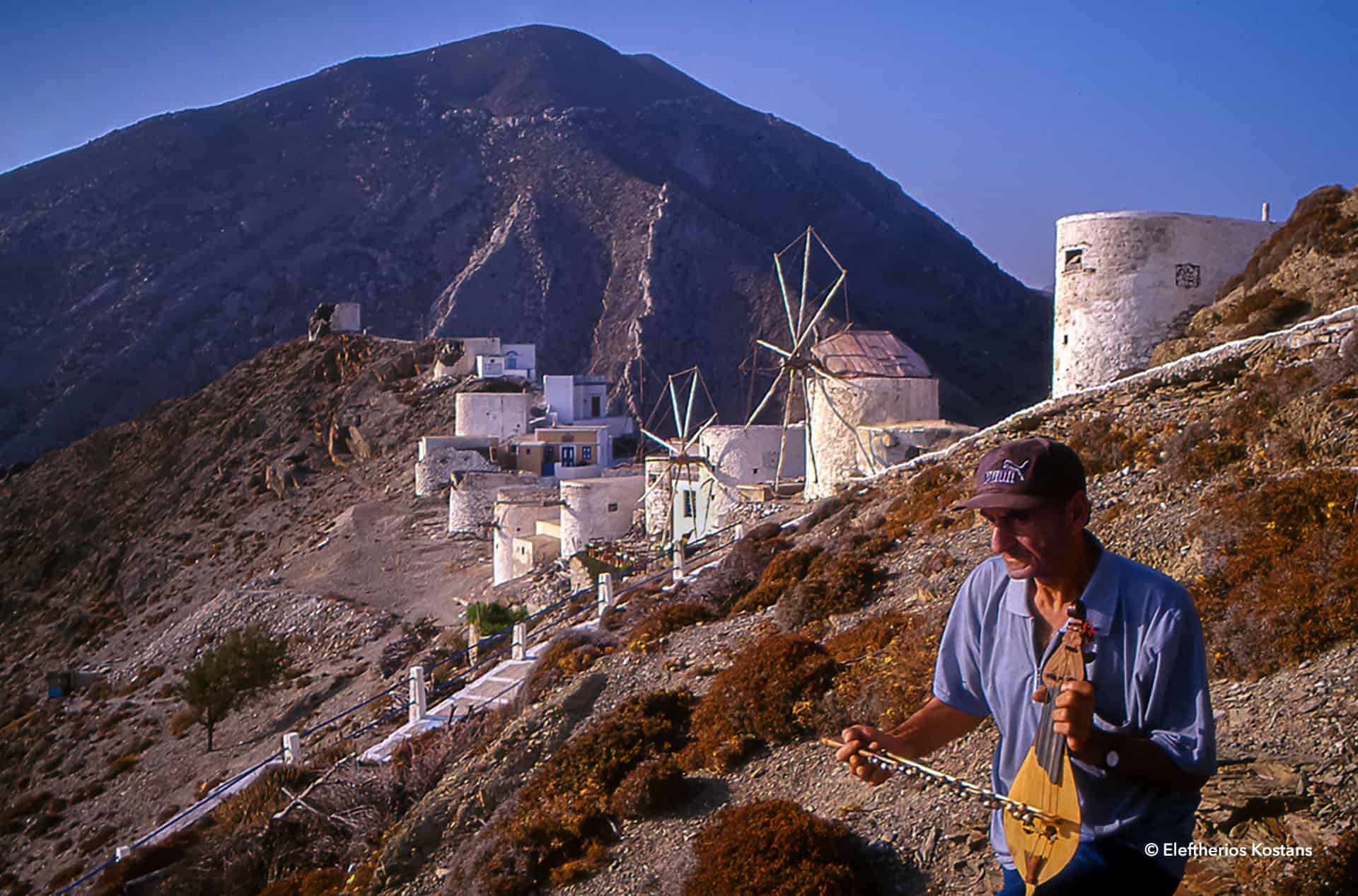 Man playing a Karpathian lyra with the old windmills and mountain backdrop of Olympos