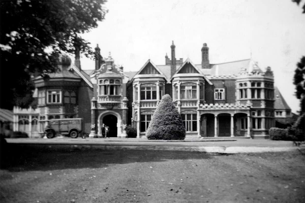 Historic photo of Bletchley Park mansion during World War II with a vehicle and people near the entrance