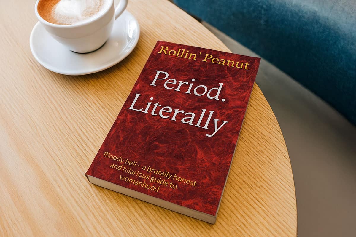 The book Period. Literally by Rollin’ Peanut resting on a wooden coffee table beside a cup of coffee.