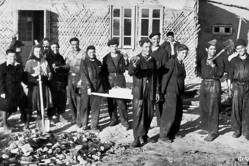Greek political refugees in Tashkent during the early 1950s working together to build wooden houses for their new Greek communities, holding tools and smiling in front of construction sites.