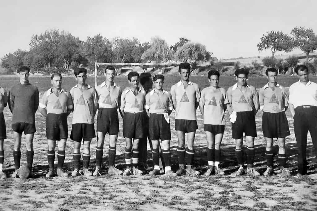 Football team of Greek political refugees from the 12th Greek community in Tashkent, early 1950s, posing on a dirt field wearing uniforms and boots.