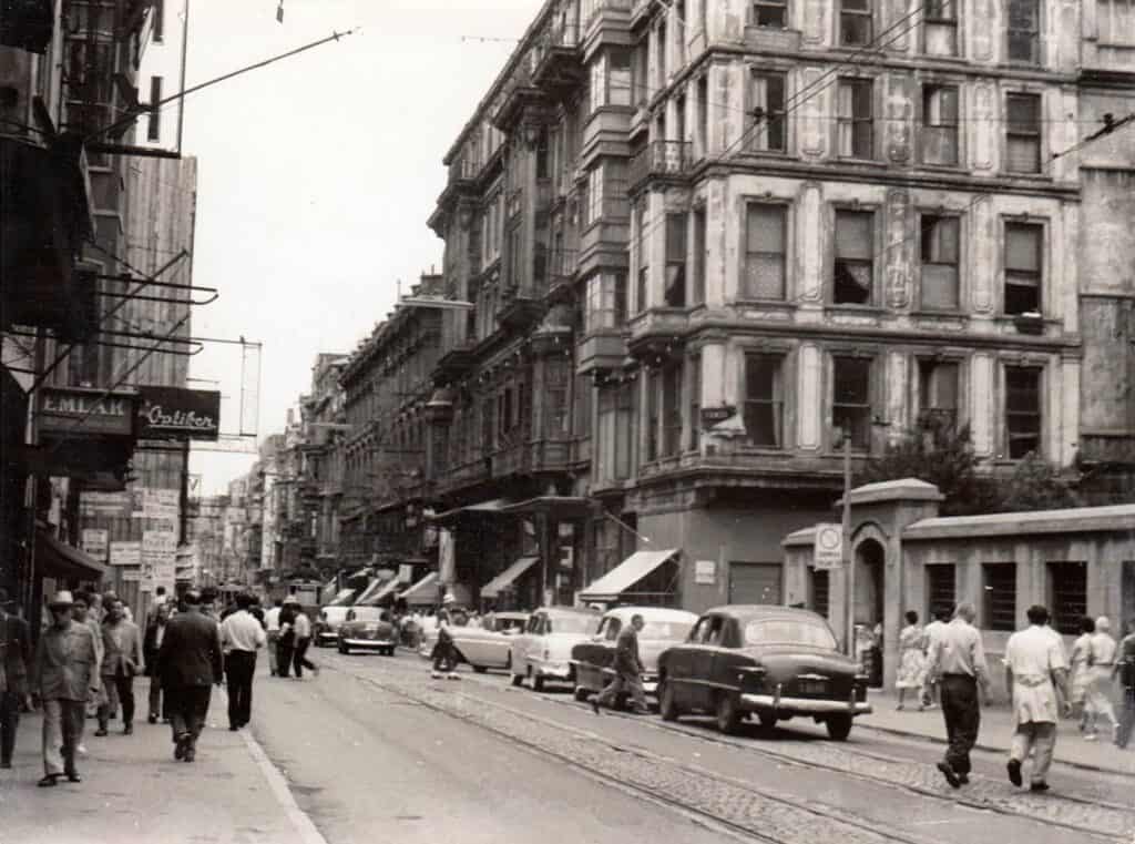 Street scene on İstiklal Caddesi in Istanbul during the late 1950s, with pedestrians, historic buildings, and vintage cars.