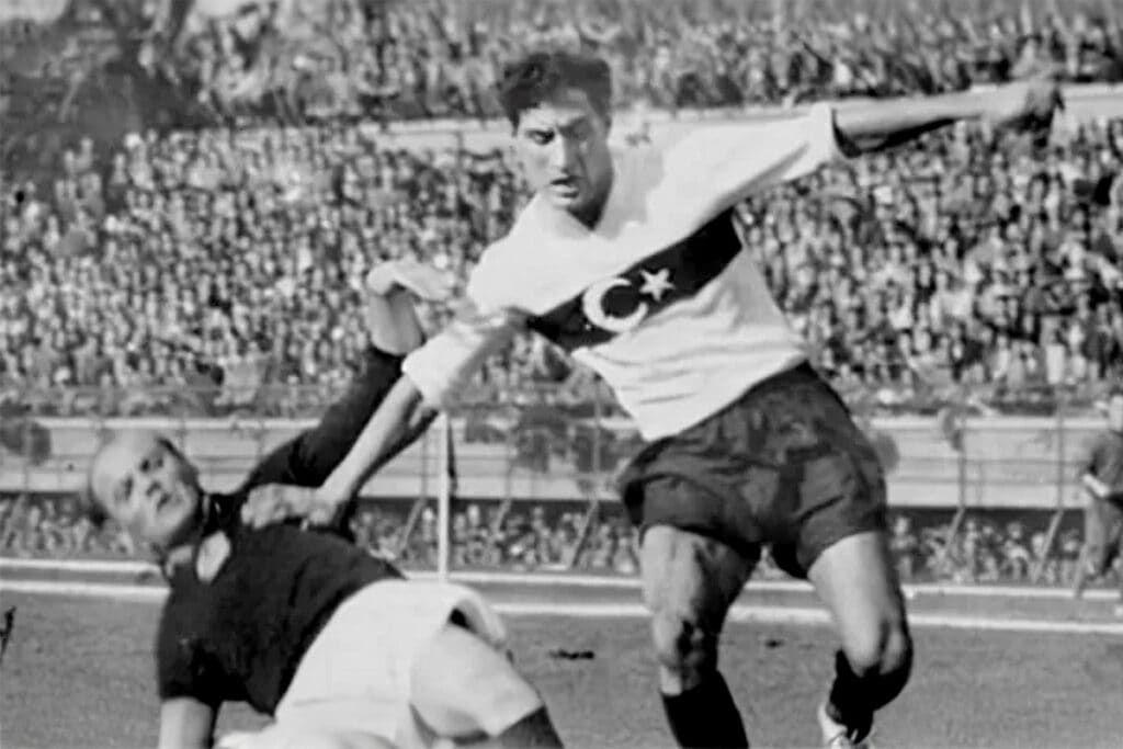 Lefter Küçükandonyadis wearing the Turkish national team jersey during a match in the 1950s, moving past an opposing player.