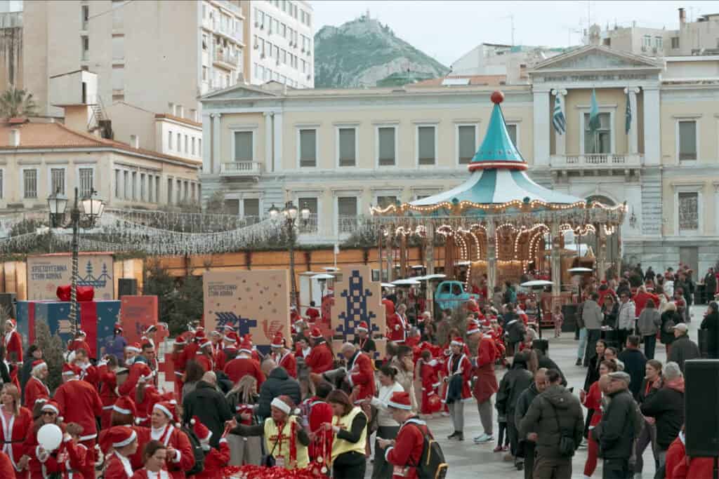 Crowds of runners dressed as Santa Claus gather at Kotzia Square near a Christmas market in central Athens