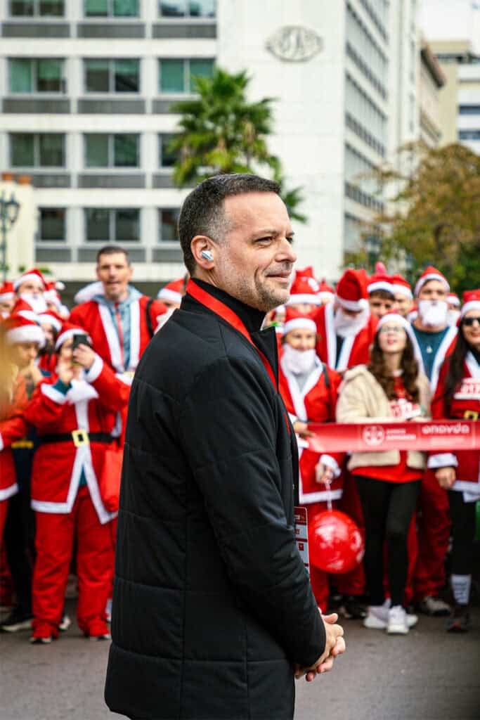 Athens Mayor Haris Doukas standing near the start of the Athens Santa Run, surrounded by runners dressed as Santa Claus