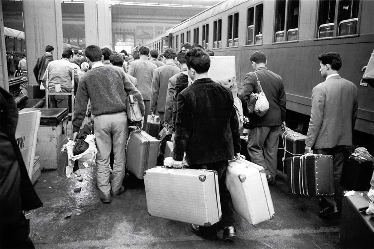 Guest workers arriving at Munich Central Station in the 1960s, carrying suitcases as they begin their journey as migrant laborers in West Germany