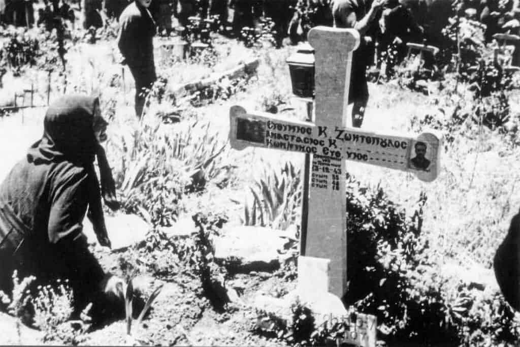 Women in Kalavryta mourning at the graves of massacre victims, with a wooden cross bearing names and dates.
