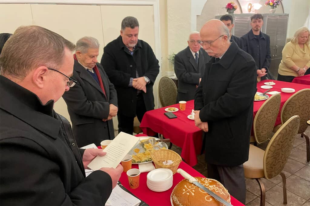 Society members stand for prayer before the Vasilopita cutting at the community hall.