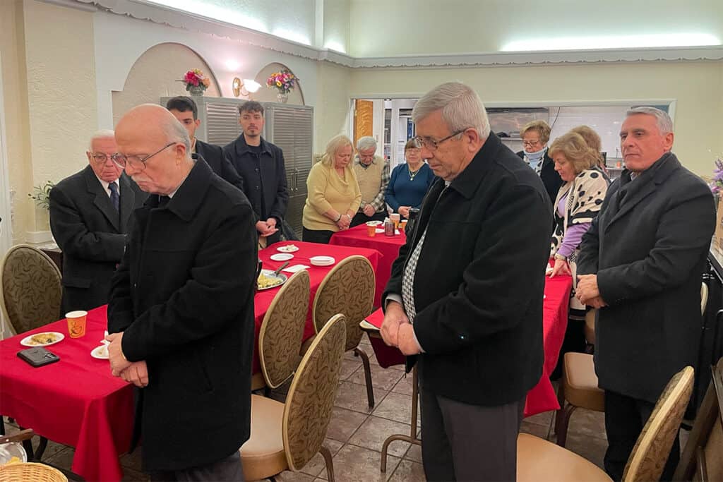 Society members stand for prayer before the Vasilopita cutting.