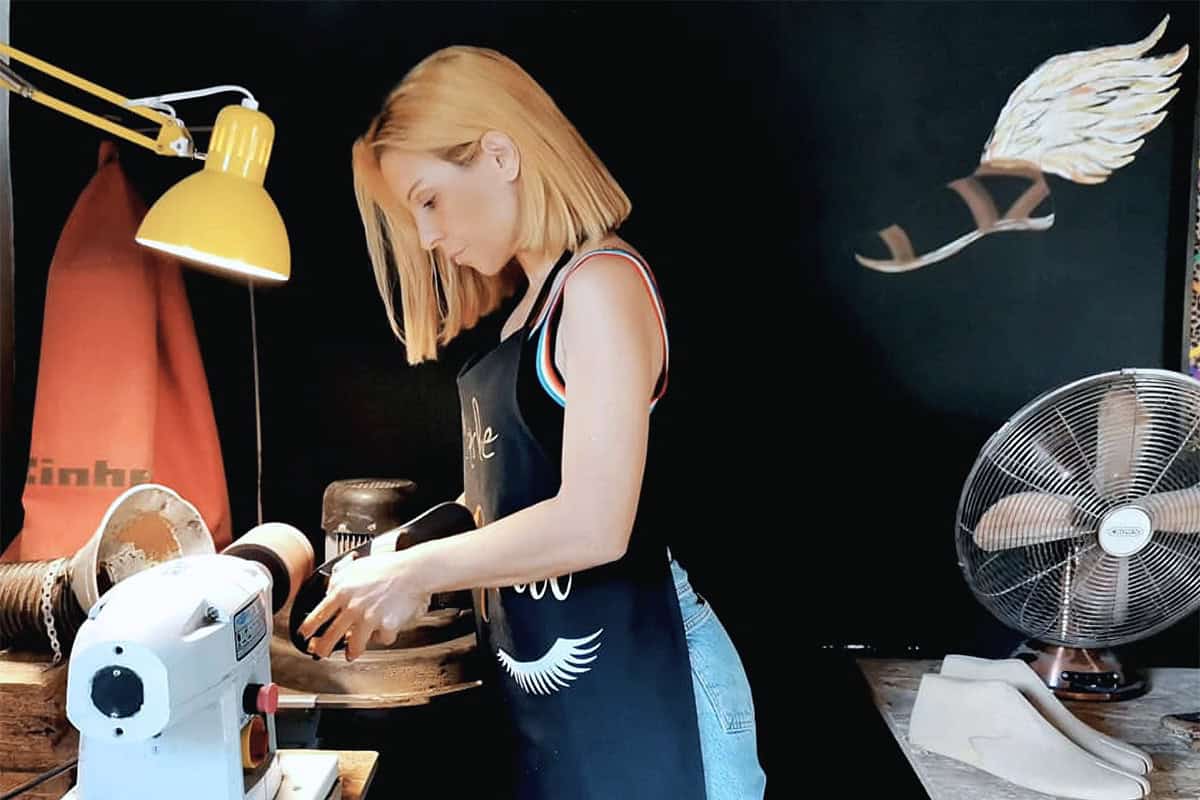 A sandal artisan works by hand in a small Athens workshop, shaping leather using traditional tools.