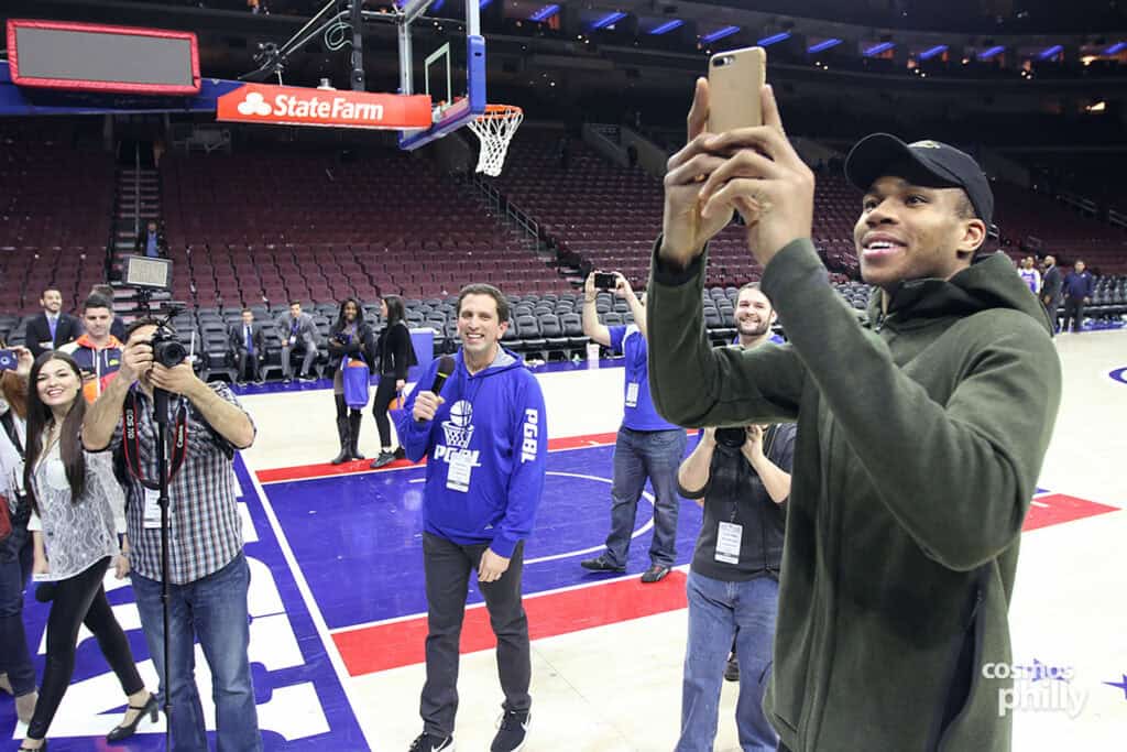 An NBA player takes a selfie on the court with organizers and photographers following Greek Heritage Night in Philadelphia.