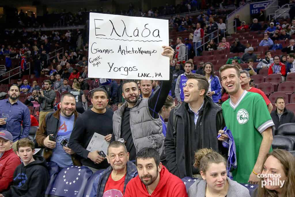 Fans in the stands hold a handmade sign in Greek celebrating Greek Heritage Night at a Philadelphia 76ers game.