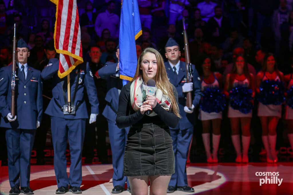 A young singer performs the national anthem at center court as a military color guard stands behind her during Greek Heritage Night.