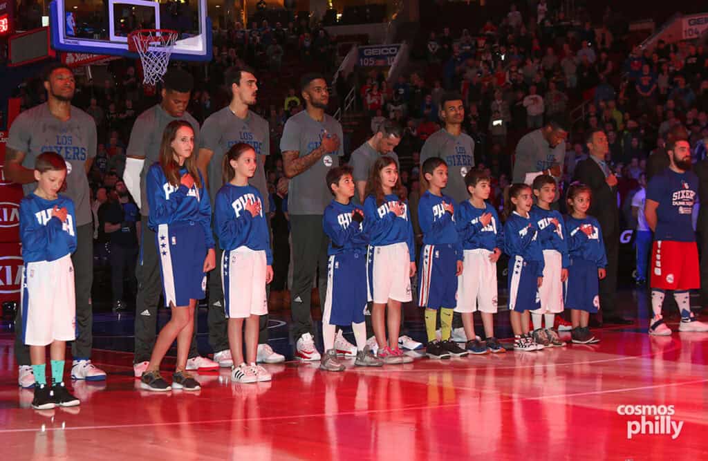Philadelphia 76ers players stand with children on the court during the national anthem at Greek Heritage Night.