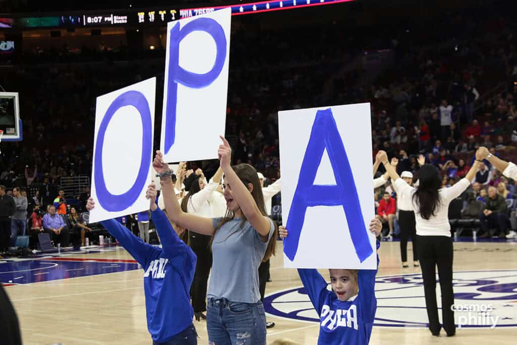 Children on the court hold large signs spelling “OPA” as part of a Greek Heritage Night celebration at a 76ers game.