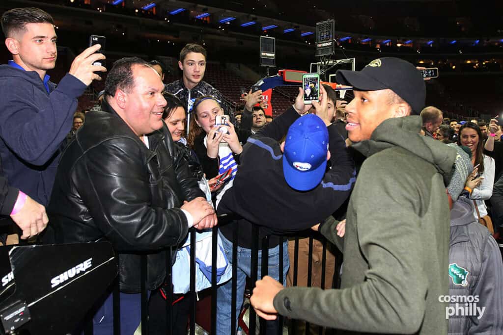 Fans gather courtside taking photos and greeting an NBA player during postgame festivities at Greek Heritage Night.