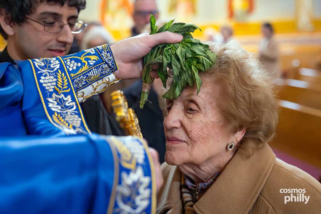 Elderly parishioner receives a Theophany blessing with basil and holy water inside the church.