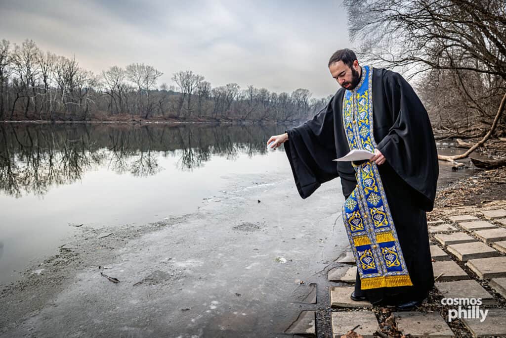 Orthodox priest reads prayers at the edge of the Schuylkill River during Theophany.