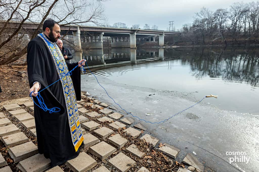 Orthodox priest holds the cross by the river as the congregation observes the ceremony.