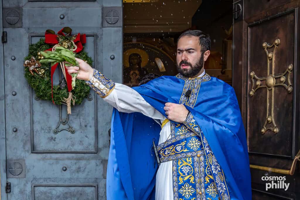 Orthodox priest blesses the church entrance with basil dipped in holy water on Theophany.