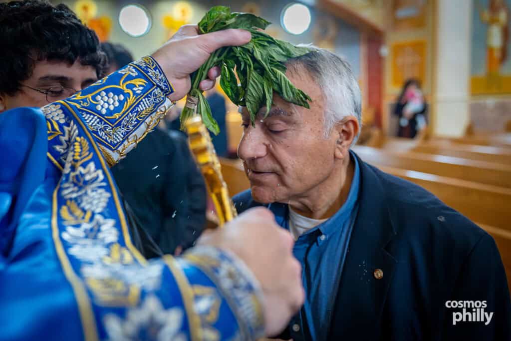 Close-up of a parishioner receiving the Theophany blessing as holy water falls from basil leaves.