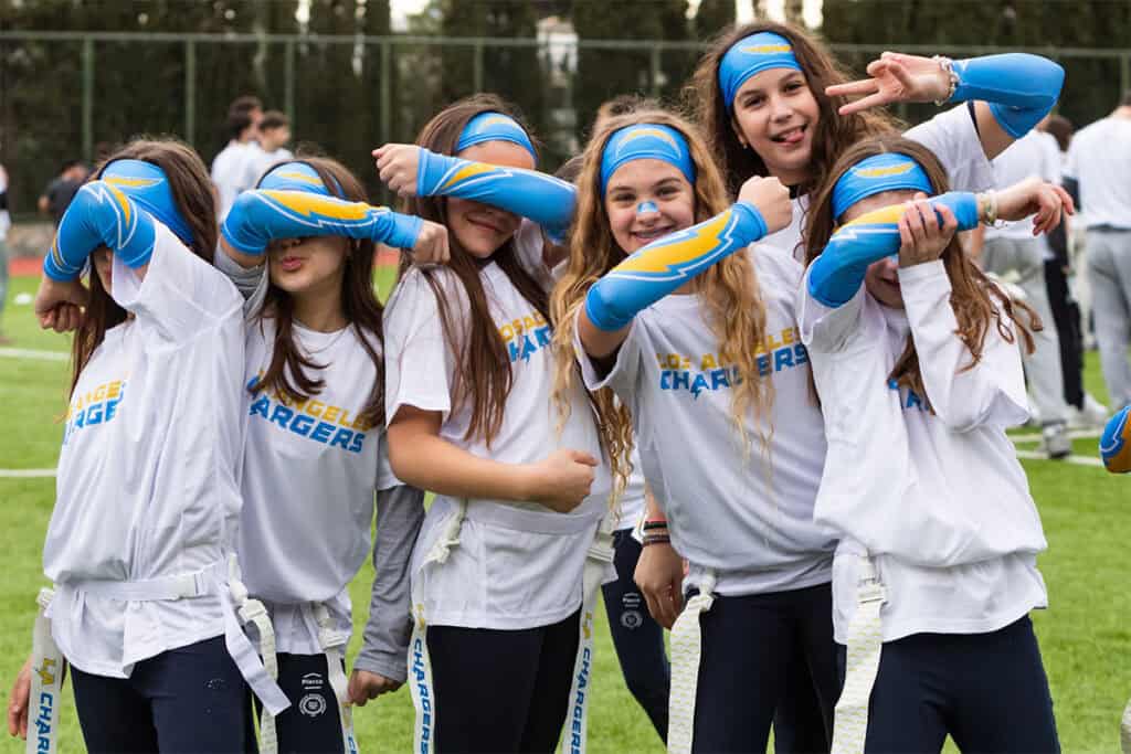Students pose and smile during a flag football camp in Athens wearing Los Angeles Chargers-themed gear.