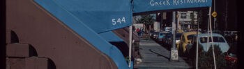 Blue awning of Symposium Greek restaurant along a city sidewalk