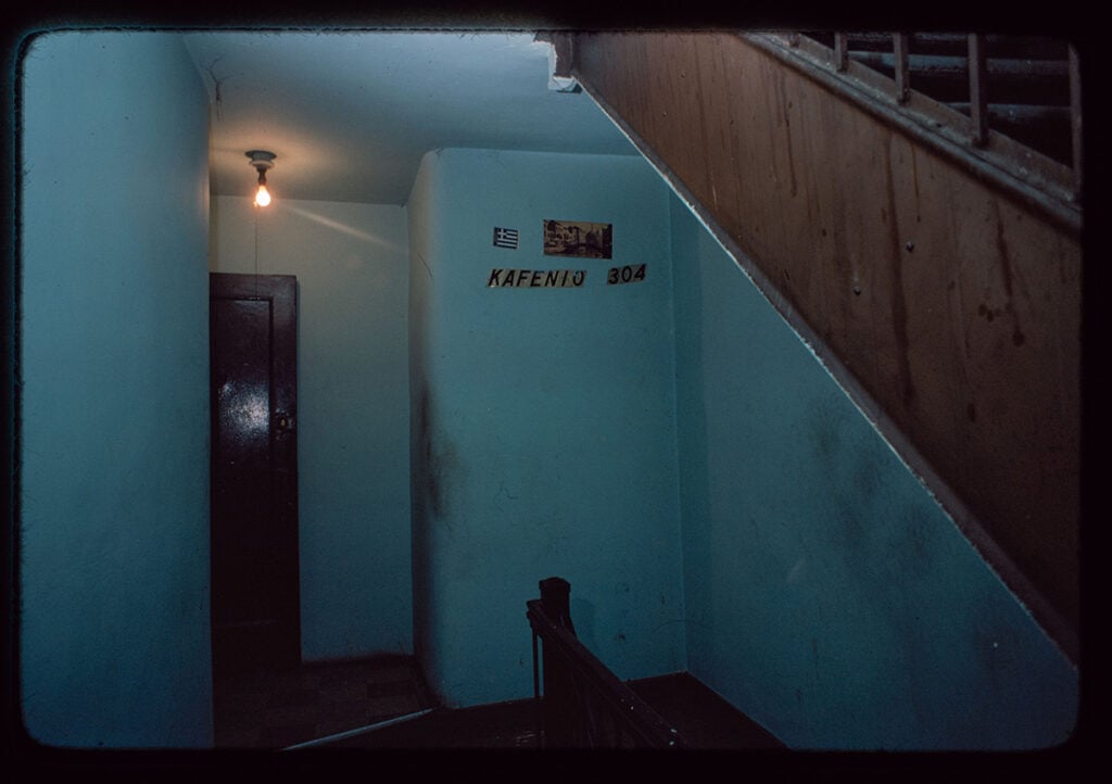 Narrow stairwell hallway with sign reading “Kafenio” and a single light bulb