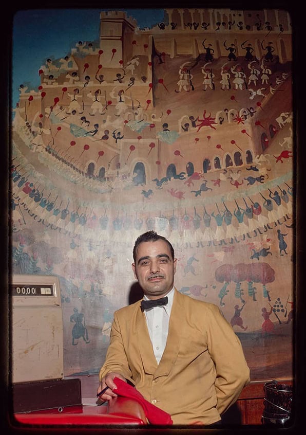 Waiter seated inside a Greek restaurant with a mural behind him