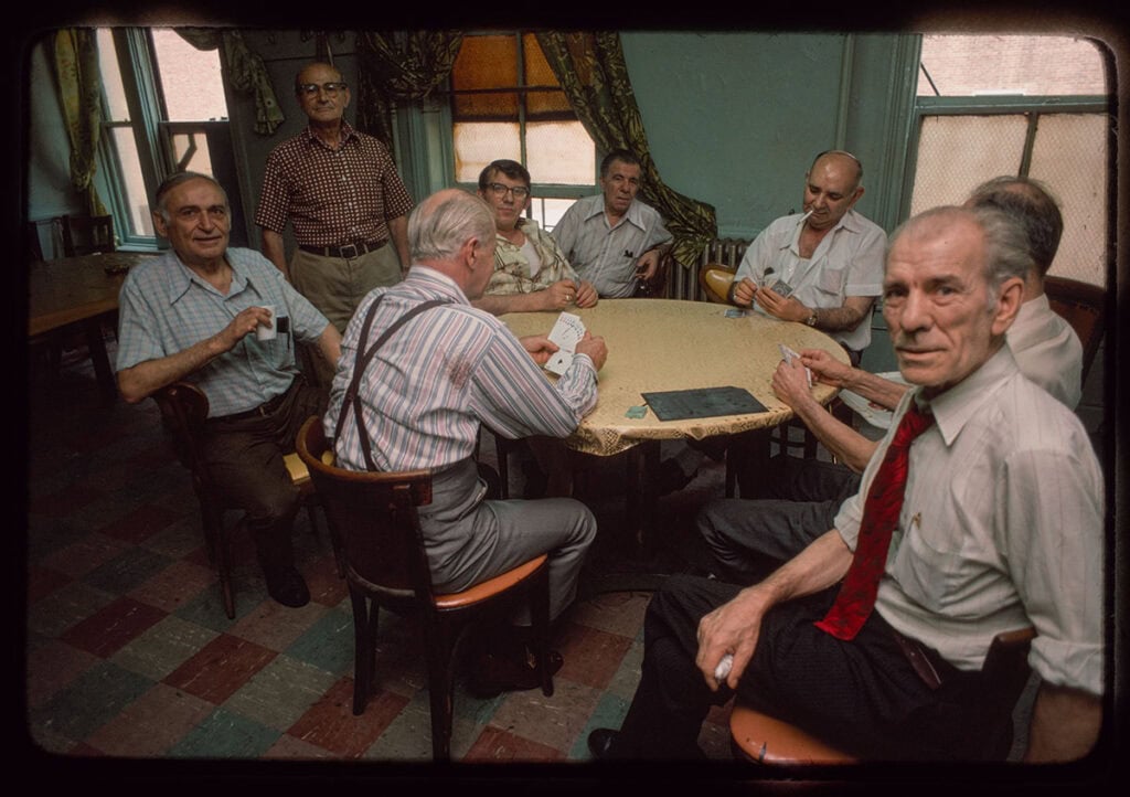 Group of older men seated around a table playing cards in a small room
