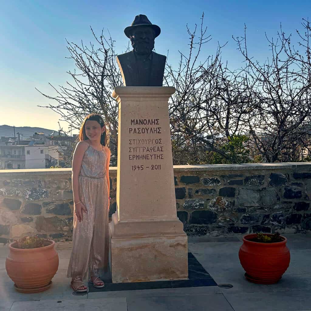 Georgia Elena standing beside the statue of Greek lyricist Manolis Rasoulis in Sises, Crete.