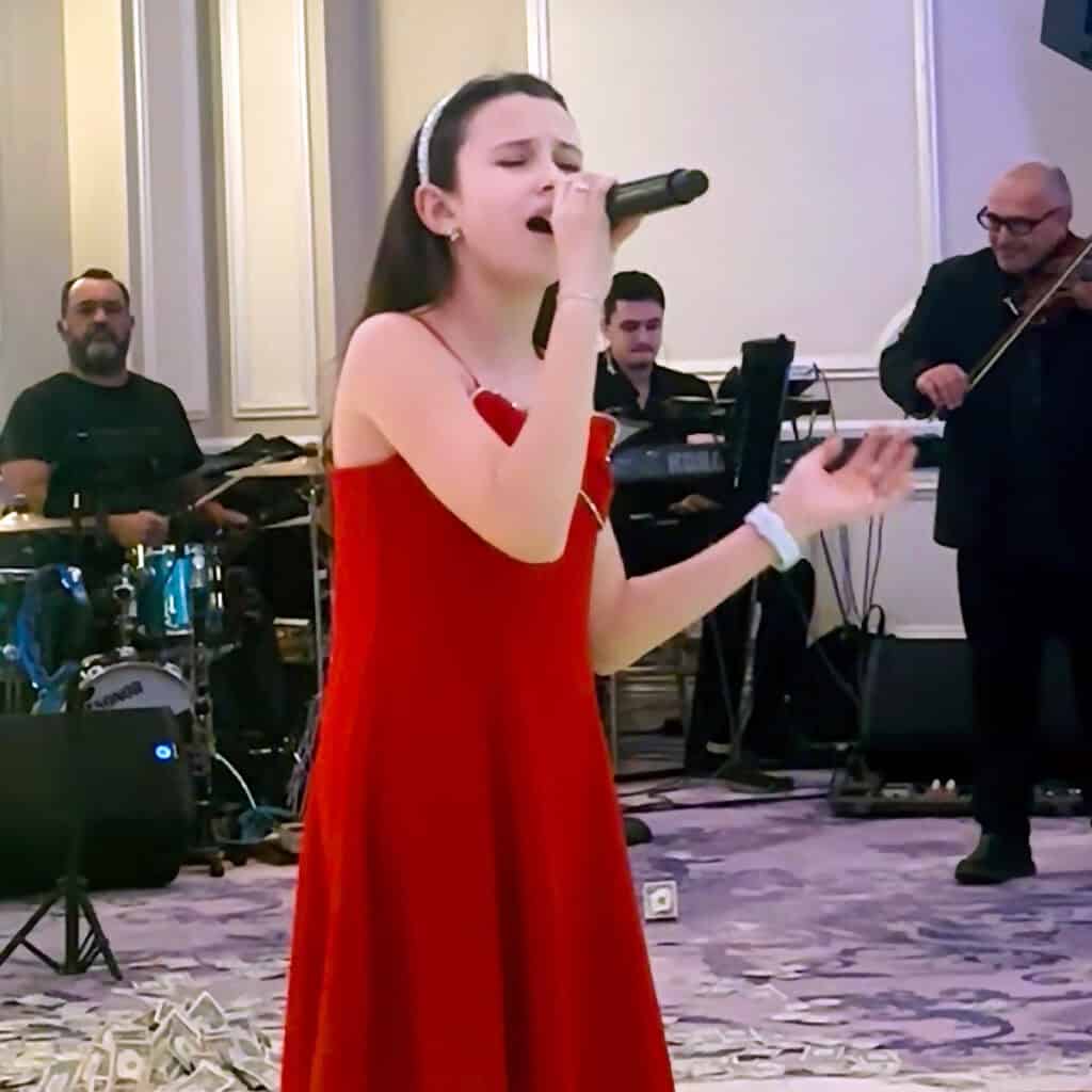 Georgia Elena singing on stage with musicians during a Greek community event.
